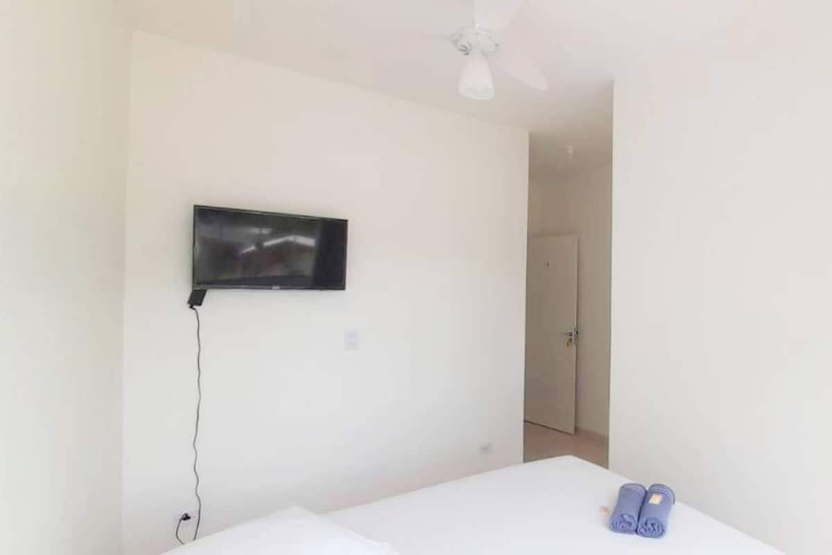 A bedroom with a bed, a TV mounted on the wall, and a ceiling fan.