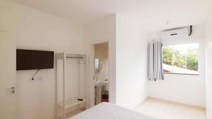 A bedroom with a bed, a television mounted on the wall, a window with curtains, and a bathroom visible through an open door. - Pousada Pontal do Sul (Pontal do Parana)