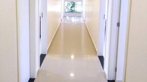 A long, narrow hallway with white walls and doors on both sides, leading to a bright room with a window at the end. - Pousada Pontal do Sul (Pontal do Parana)