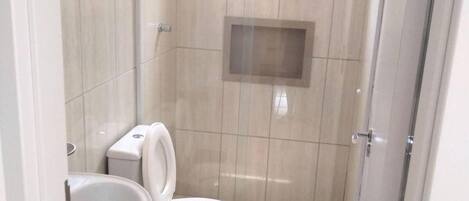 Une petite salle de bain carrelée, équipée de toilettes, d’un lavabo et d’un espace douche.