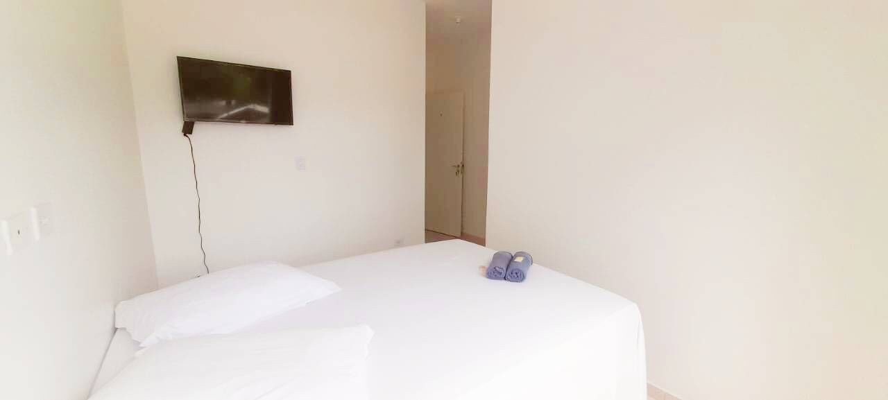Ein kleiner, einfacher Raum mit einem Einzelbett, einem an der Wand befestigten Flachbildfernseher und einer Tür zu einem weiteren Raum.