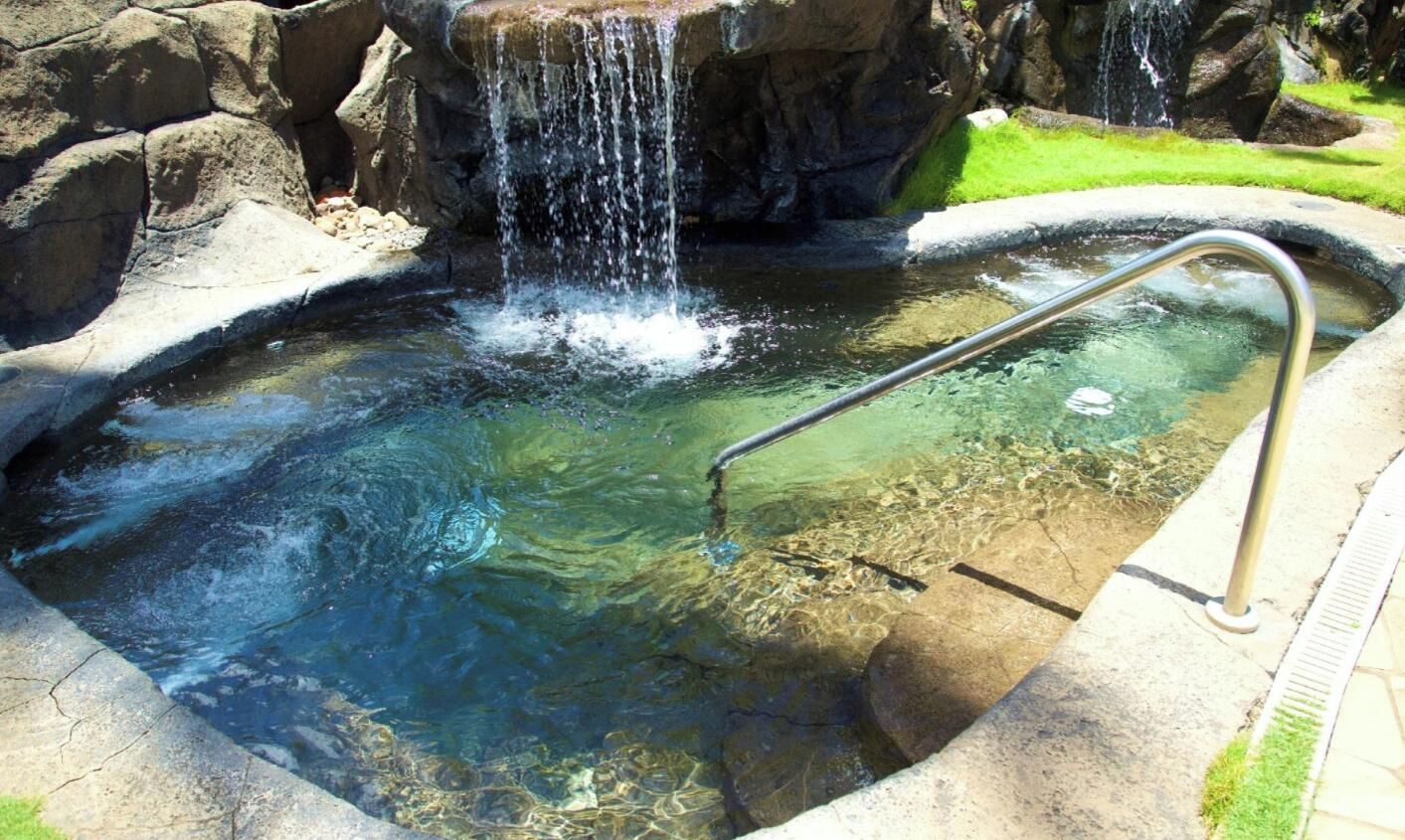 Une piscine aux eaux cristallines, dotée d’un escalier en métal et agrémentée d’une cascade.