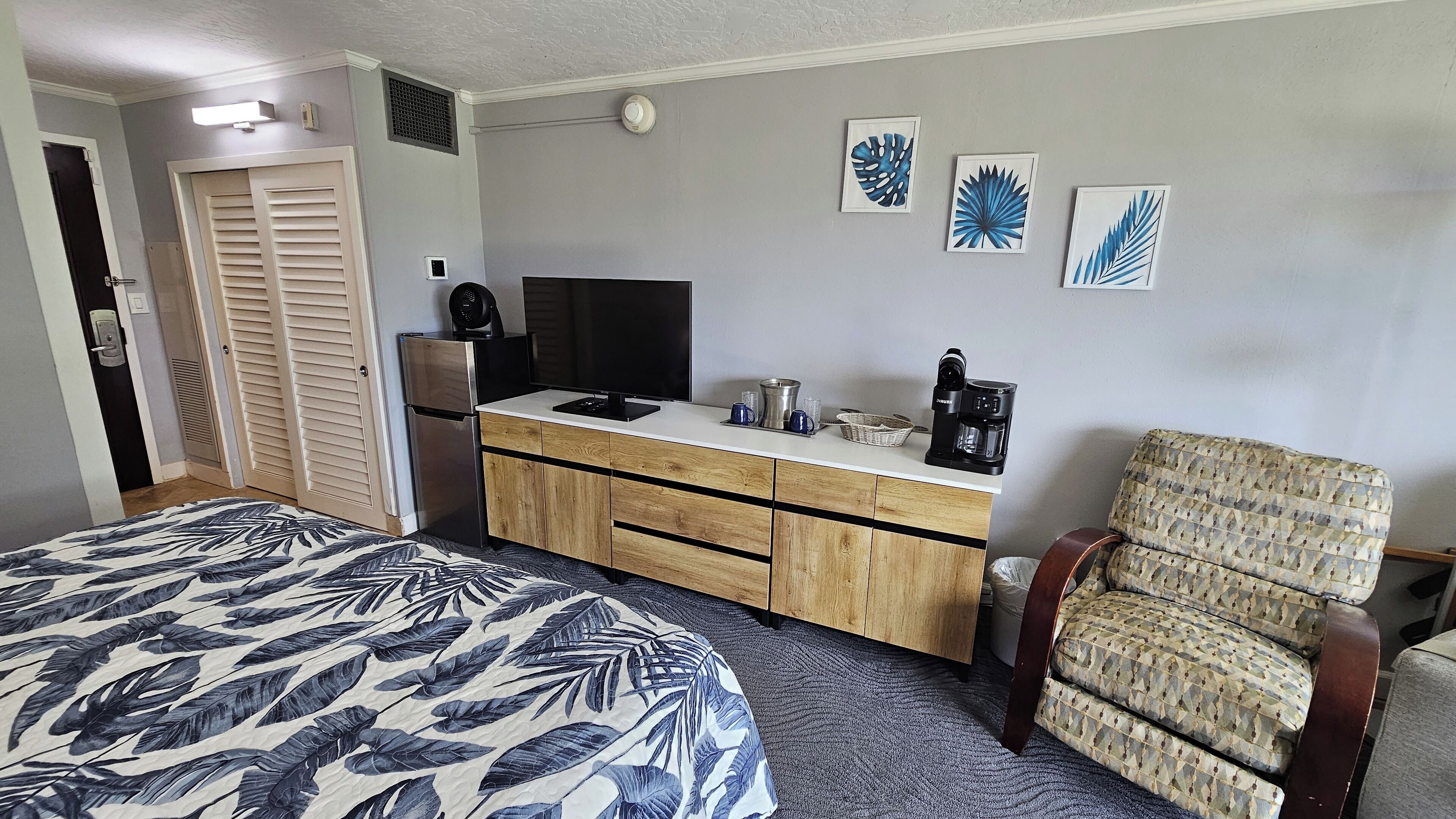 Une chambre avec un lit, un bureau, une chaise, une télévision et une machine à café.