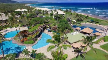 A resort with multiple swimming pools, palm trees, and a view of the ocean.