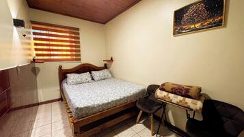 Un dormitorio con una cama de madera, un escritorio pequeño, una silla, una ventana con persianas y un cuadro en la pared.