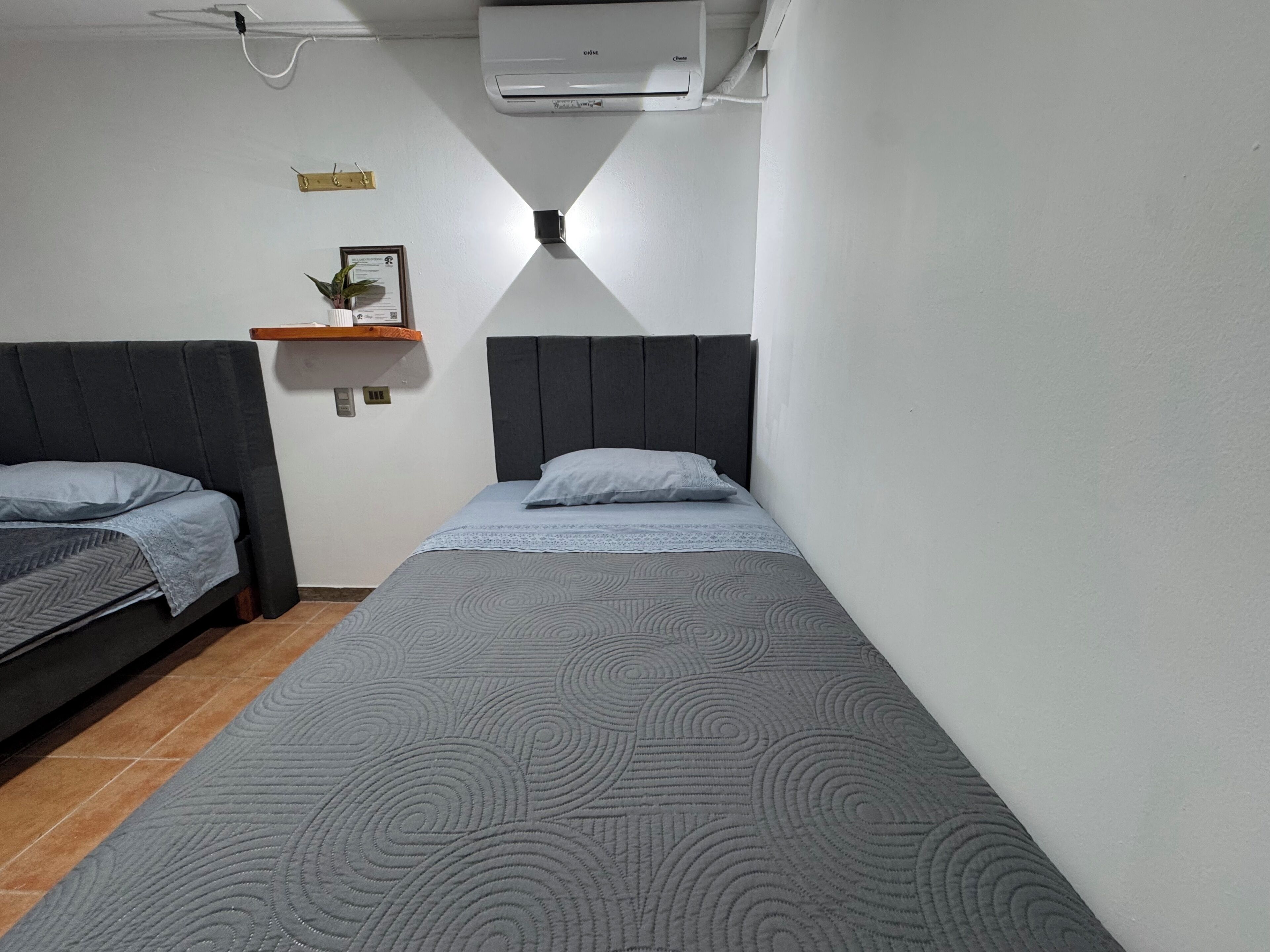 Una habitación con dos camas individuales, un estante pequeño con una planta y un equipo de aire acondicionado en la pared.