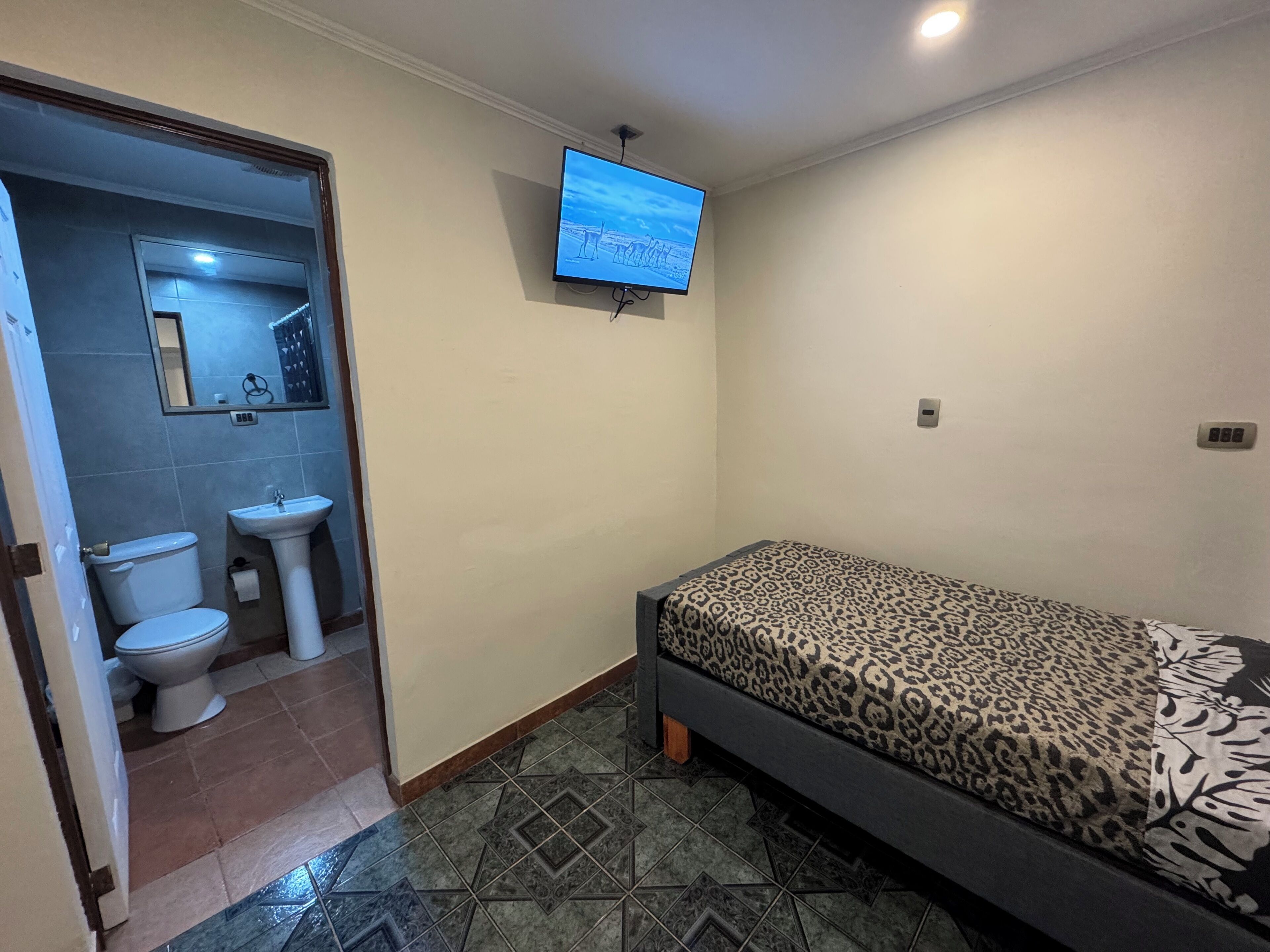Una habitación pequeña y limpia, con cama, inodoro y lavamanos.