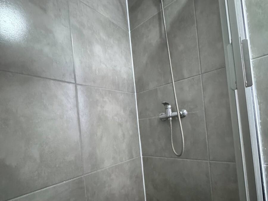 A shower with a handheld showerhead and a wall-mounted faucet in a tiled bathroom.