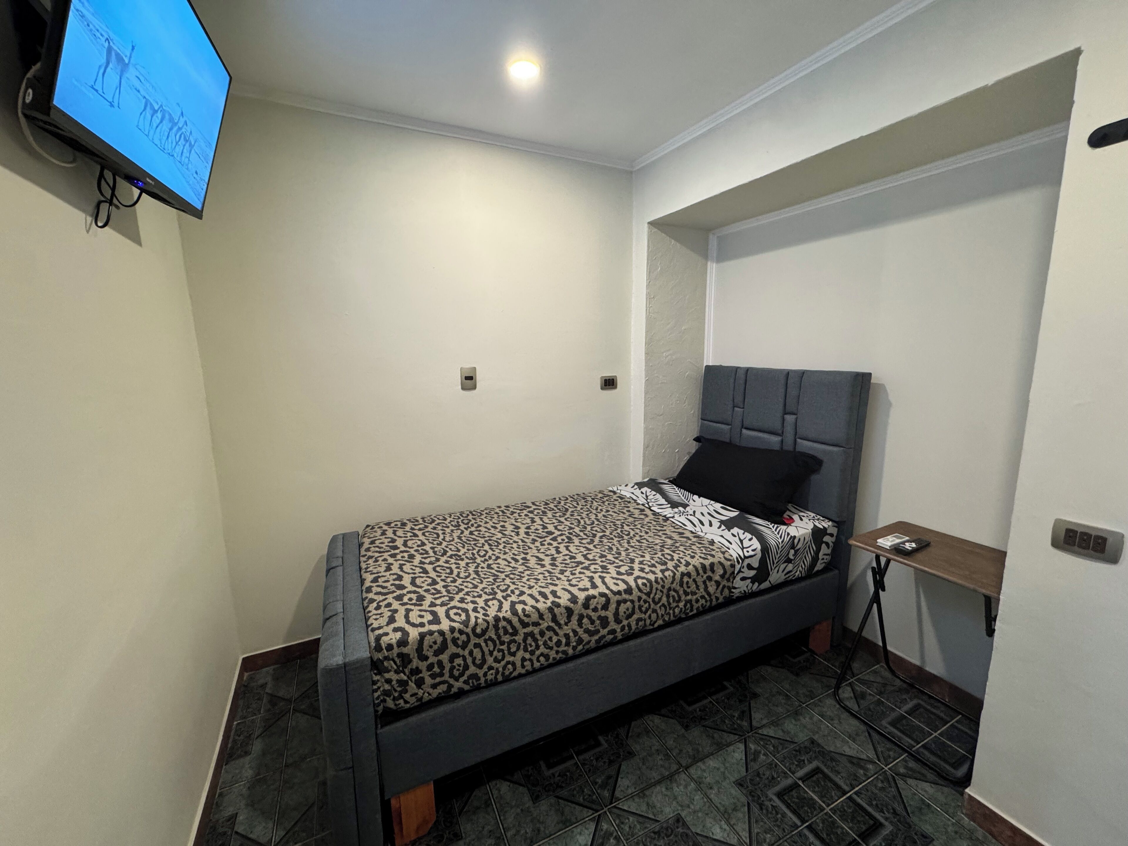 Un dormitorio pequeño y moderno con cama, mesita de noche y televisor montado en la pared.