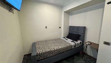 Un dormitorio pequeño y moderno con cama, mesita de noche y televisor montado en la pared.