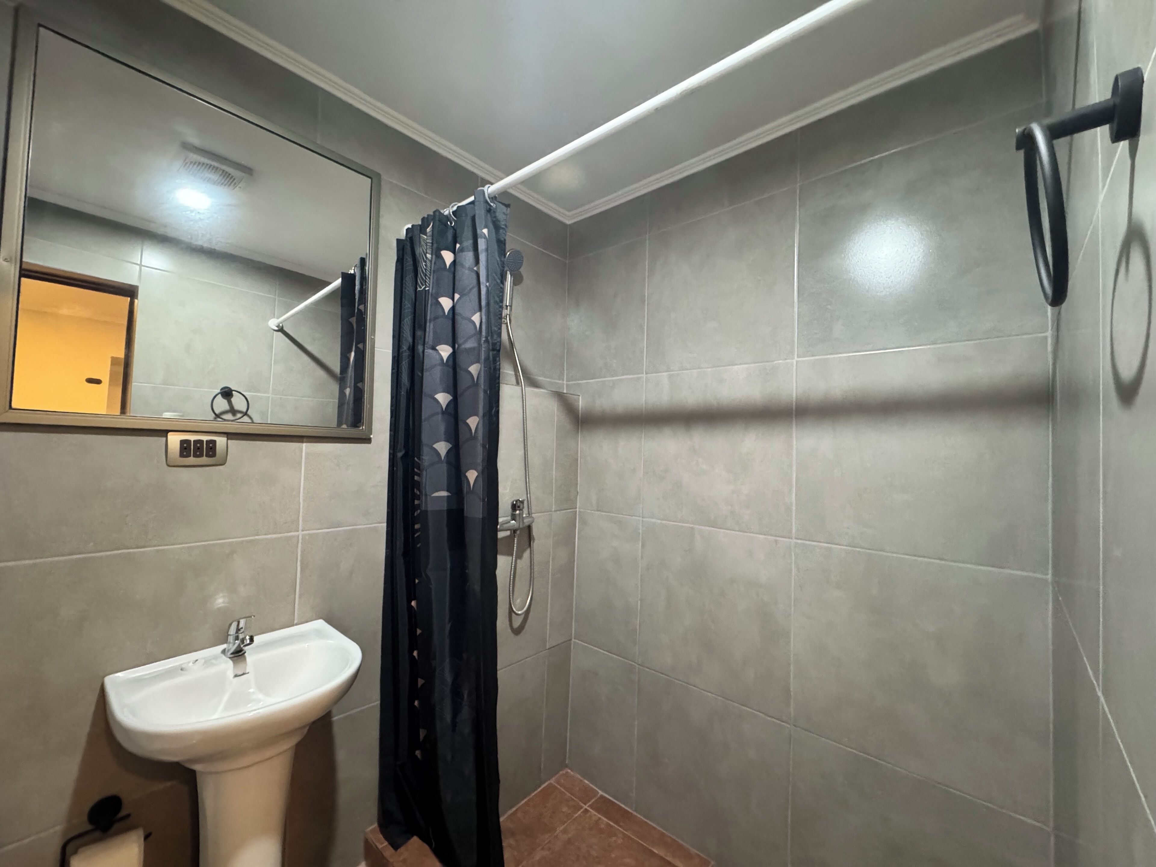 Un bany amb un lavabo blanc, un mirall i una dutxa amb cortina negra.