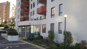 Un edificio de apartamentos moderno con fachada blanca, balcones rojos y un estacionamiento con el símbolo de una bicicleta.