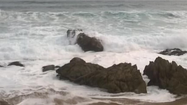 Una playa con olas rompiendo contra rocas grandes.