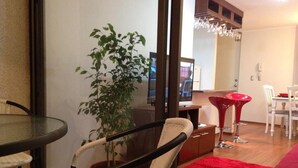 Un comedor con una mesa de vidrio, sillas de mimbre, una alfombra roja y una planta en maceta.