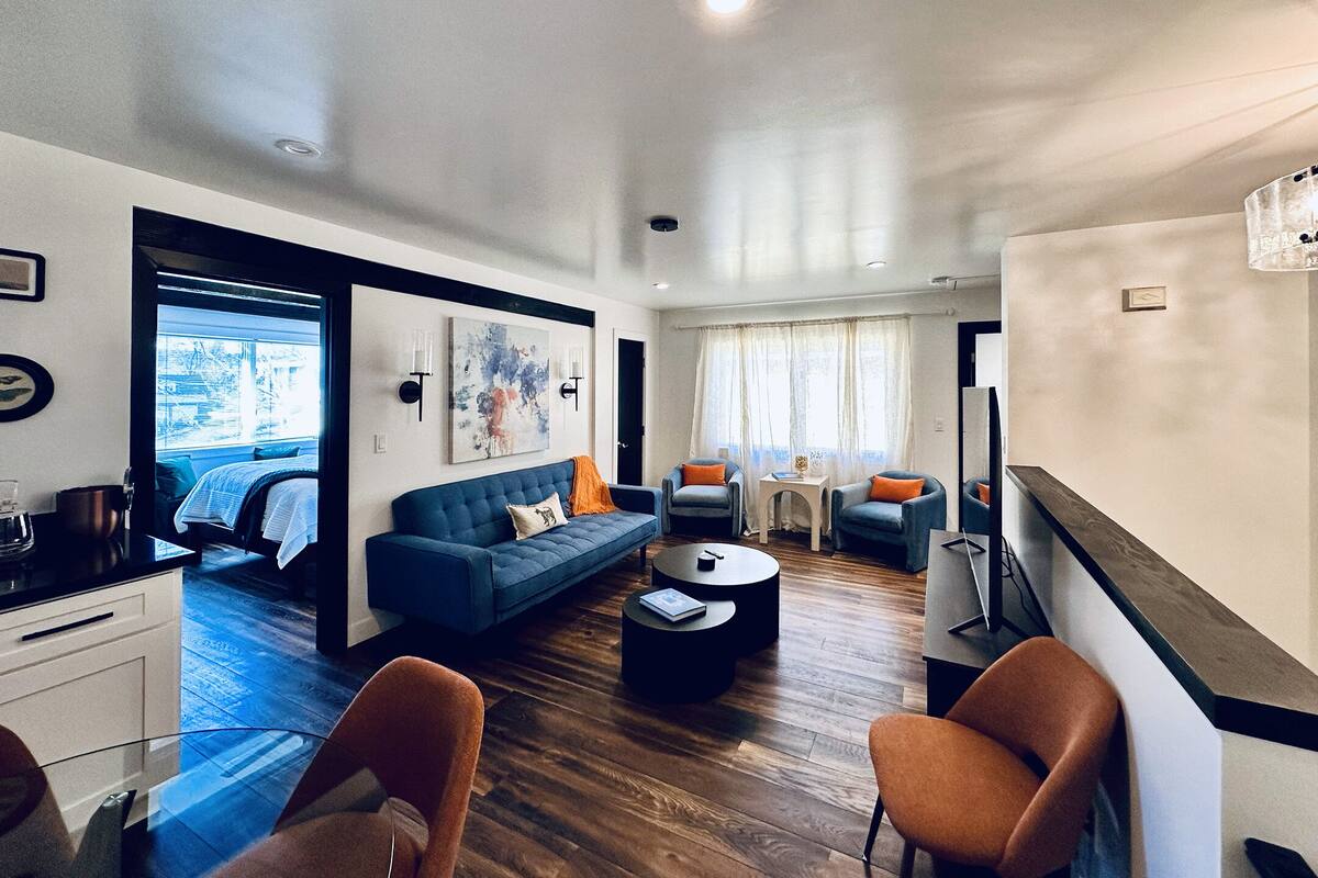 A modern living room with a blue sofa, two armchairs, a coffee table, and a dining area with a table and chairs.