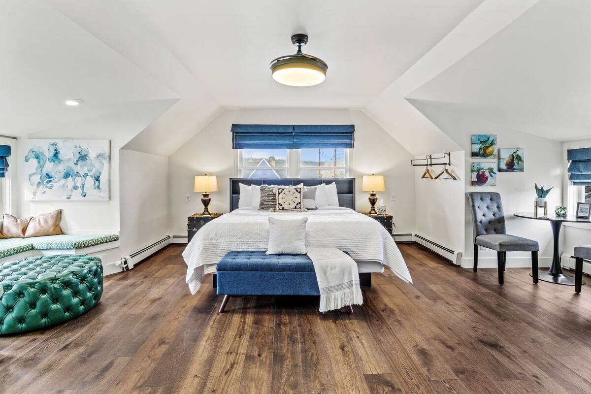 A spacious bedroom with a large bed, a blue bench, a chair, and a dining table.