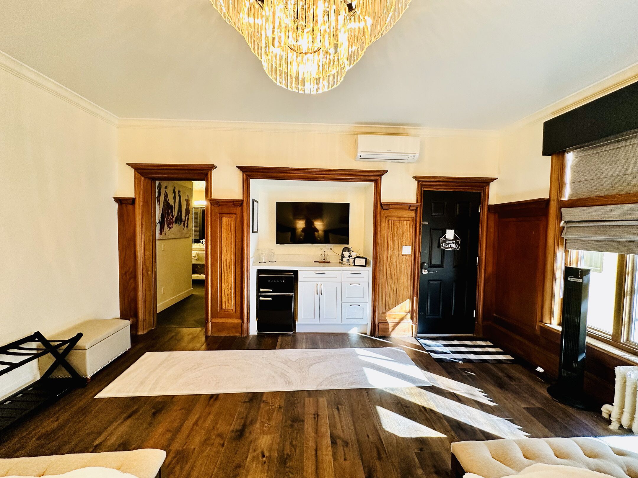Ein geräumiges Wohnzimmer mit Holzböden, einer großen Kronleuchter und Blick in die Küche.