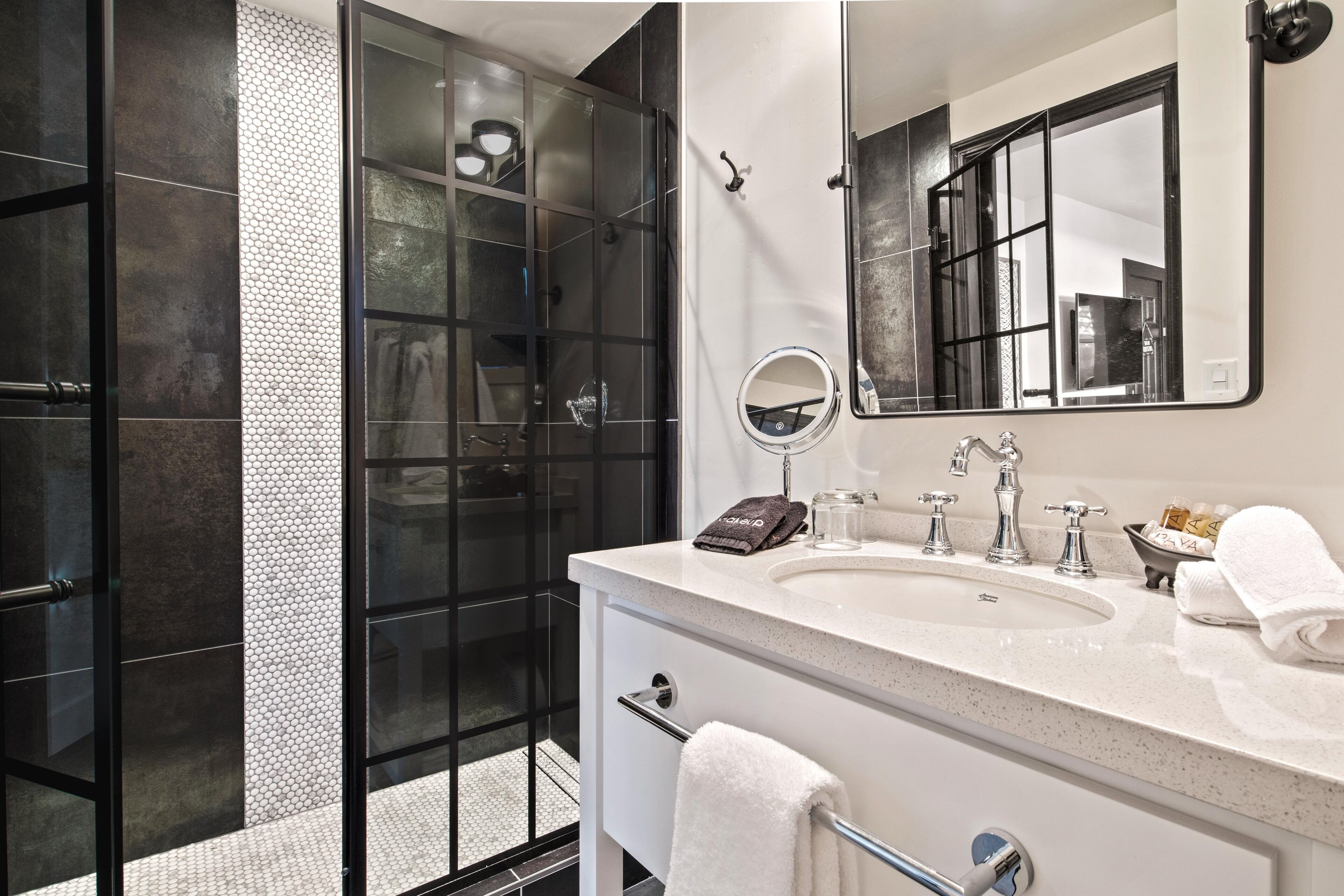 A modern bathroom with a glass shower enclosure, a large mirror, a white sink, and a towel rack.