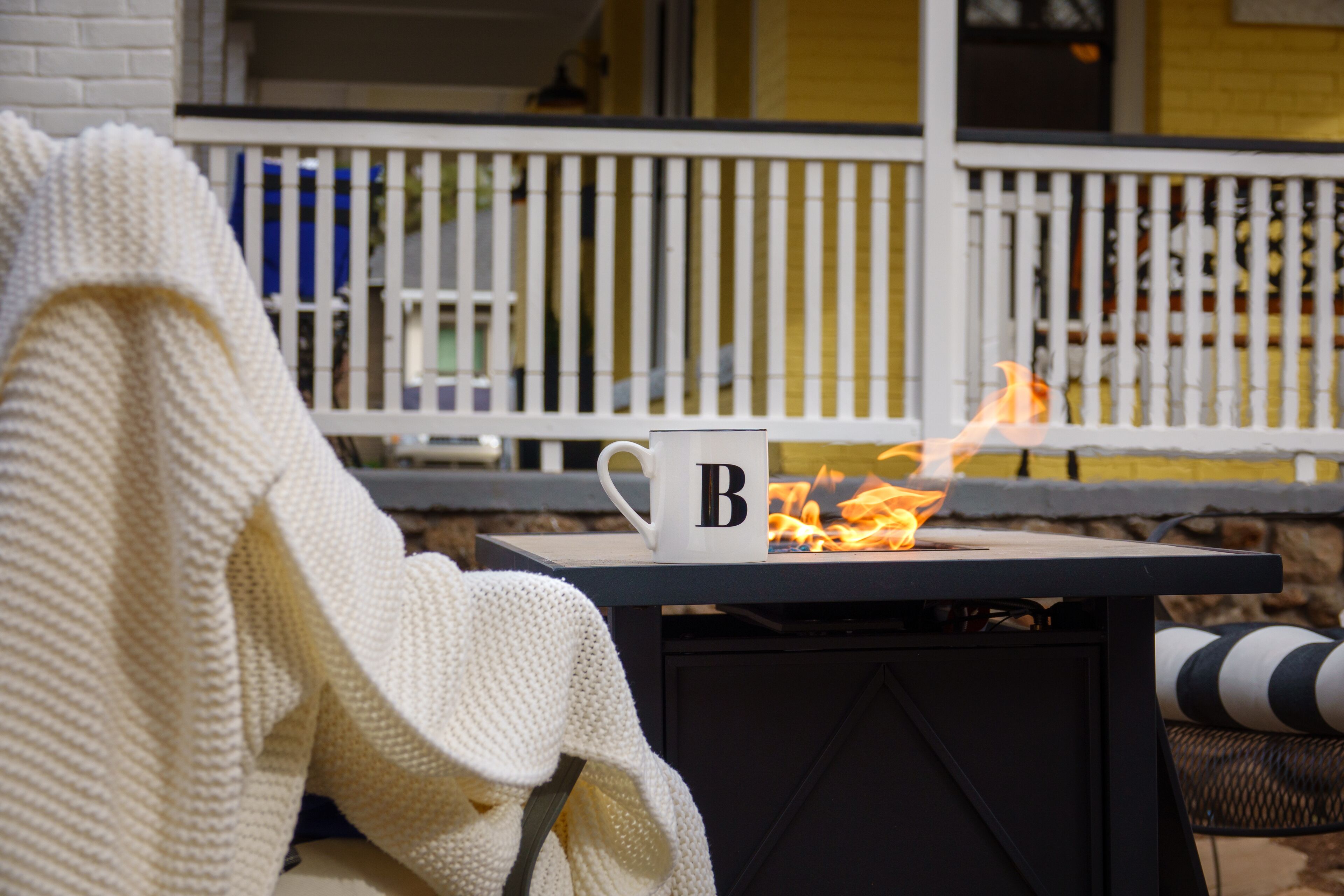 A cozy outdoor seating area with a table, a white mug with a letter, and a fire.