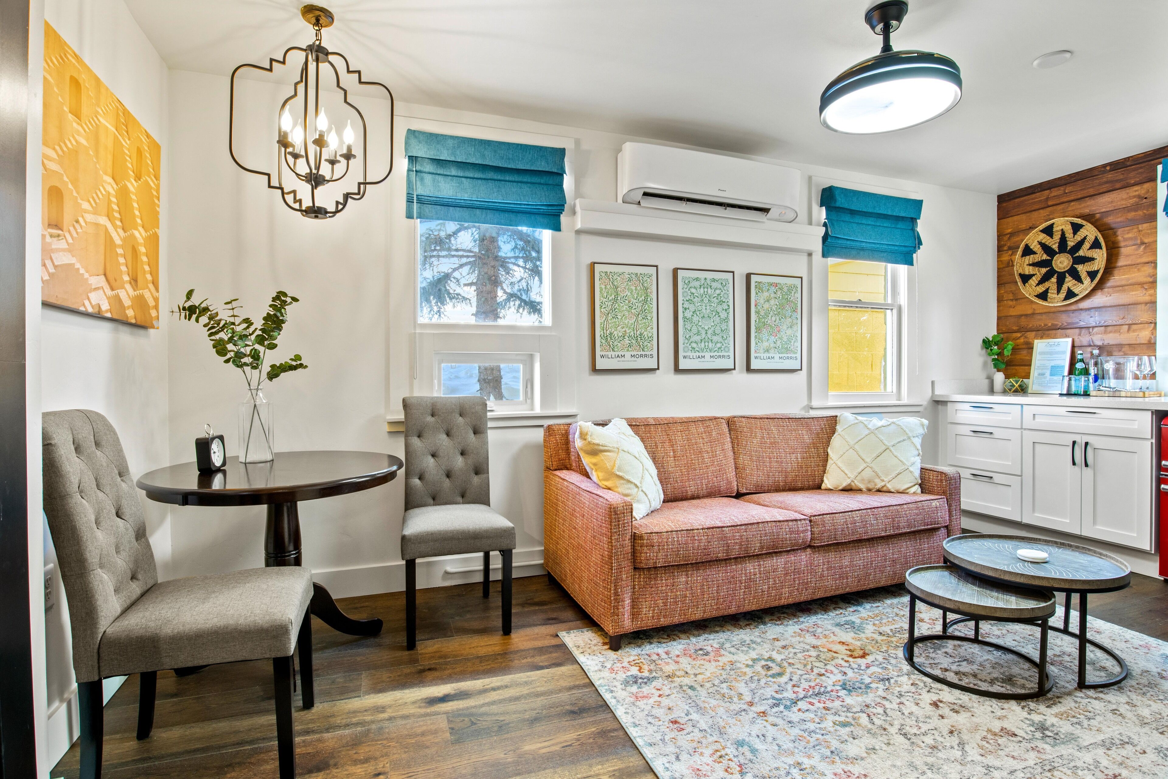 Un salon comprenant un canapé, deux fauteuils, une petite table et une table basse. Il y a une fenêtre avec des rideaux bleus, un lustre et un climatiseur fixé au mur.