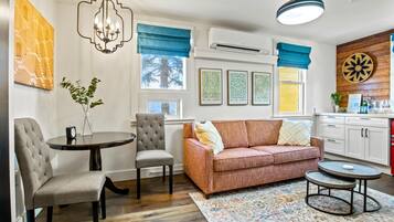 Un salon comprenant un canapé, deux fauteuils, une petite table et une table basse. Il y a une fenêtre avec des rideaux bleus, un lustre et un climatiseur fixé au mur.