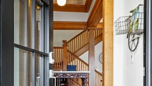 Un couloir avec un tapis à motifs noir et blanc, un plancher en bois, un escalier avec des rampes en bois et une étagère murale ornée de plantes.