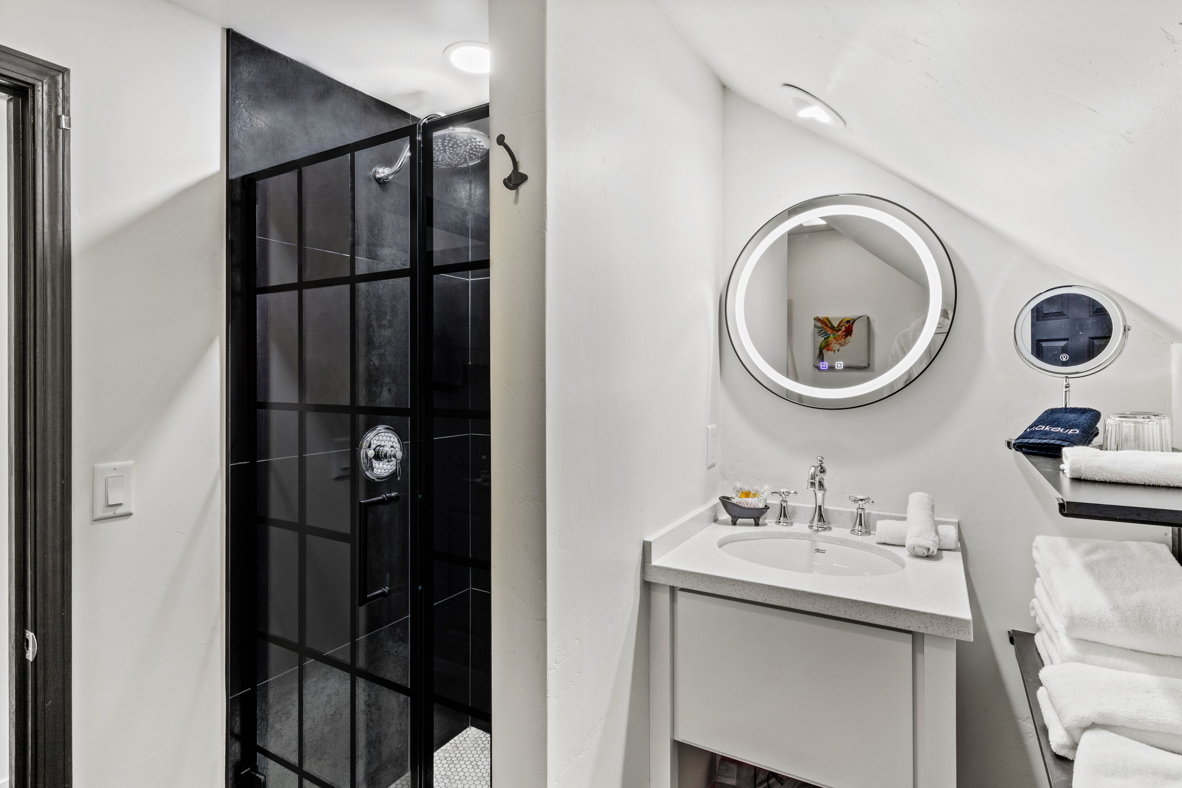 A modern bathroom with a black glass shower enclosure, a white sink with a mirror, and neatly stacked towels.
