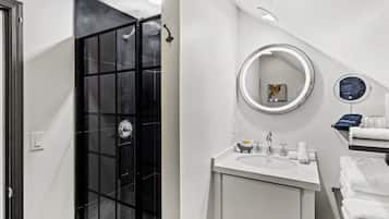 A modern bathroom with a black glass shower enclosure, a white sink with a mirror, and neatly stacked towels.