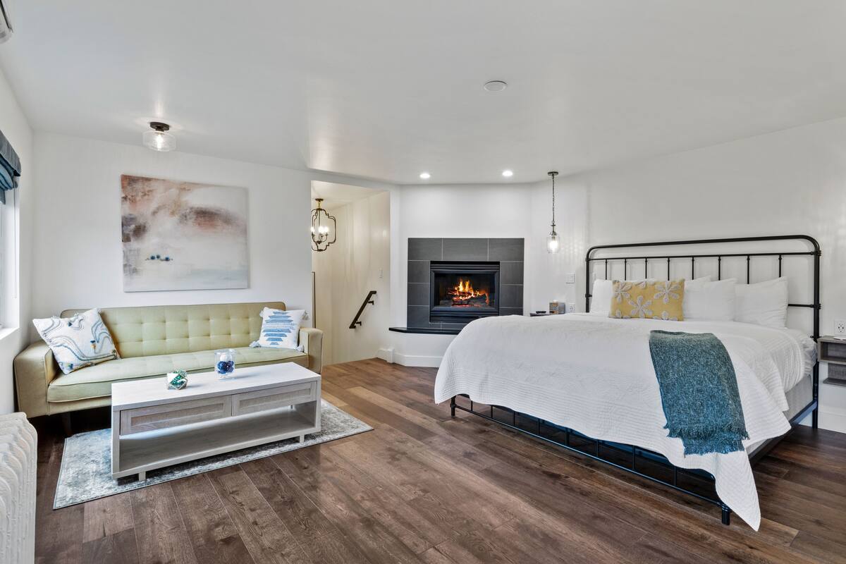 A modern bedroom with a bed, a sofa, a fireplace, and a staircase.