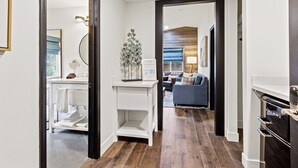 Un couloir avec une coiffeuse blanche, un miroir et une plante décorative. On aperçoit un canapé bleu au fond.