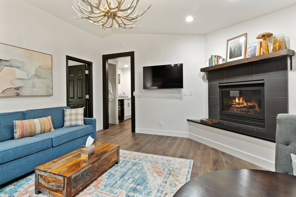 A modern living room with a blue sofa, a wooden coffee table, a fireplace, and a mounted TV.