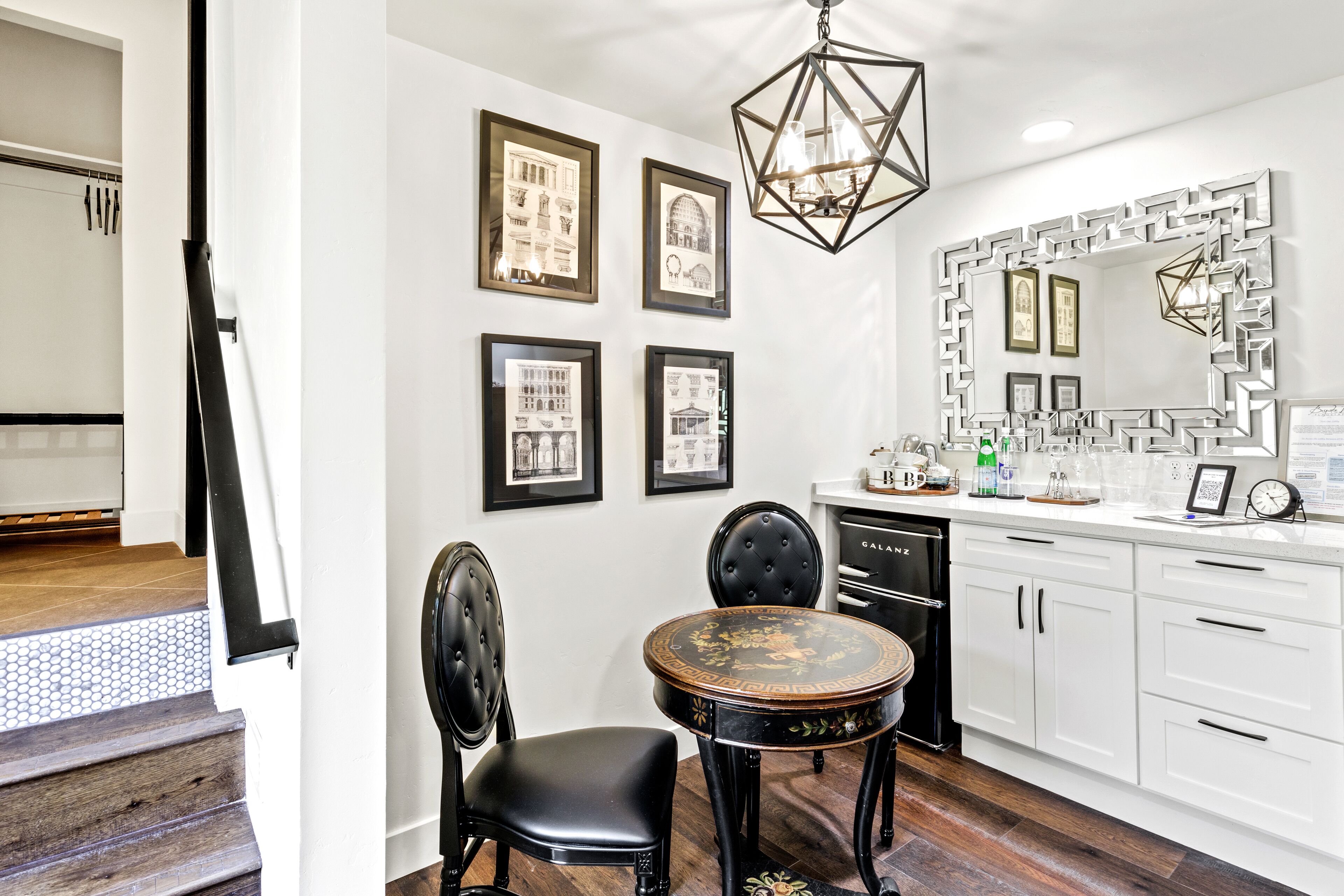 A modern kitchen with white cabinets, a black dining table, and a decorative mirror.