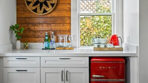 Une cuisine avec des meubles blancs, un réfrigérateur Galanz rouge, un mur en bois orné d’une assiette décorative et une fenêtre donnant sur un paysage verdoyant.