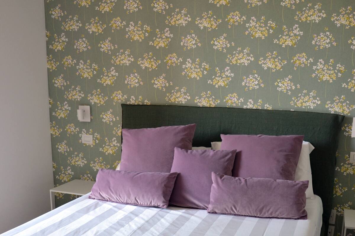 A bed with a striped bedspread, a green headboard, and purple pillows.