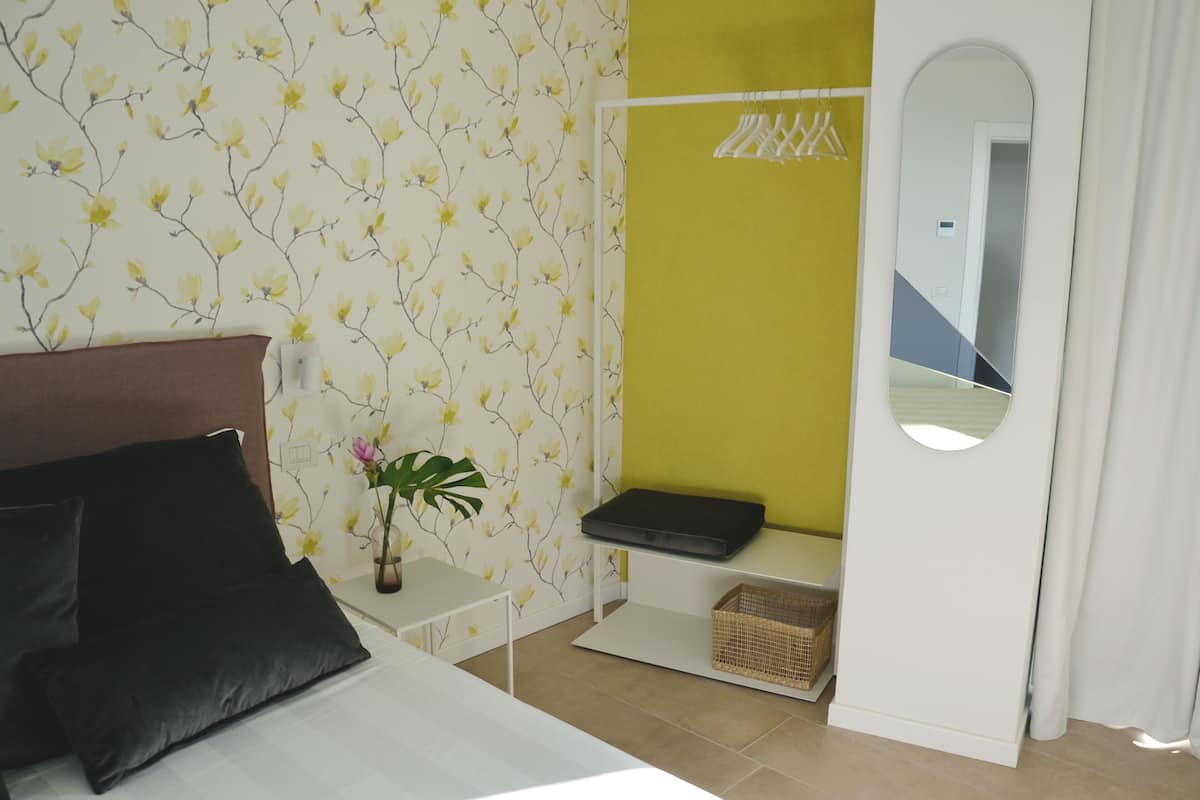 A bedroom with a bed, a bedside table, a mirror, and a small plant.