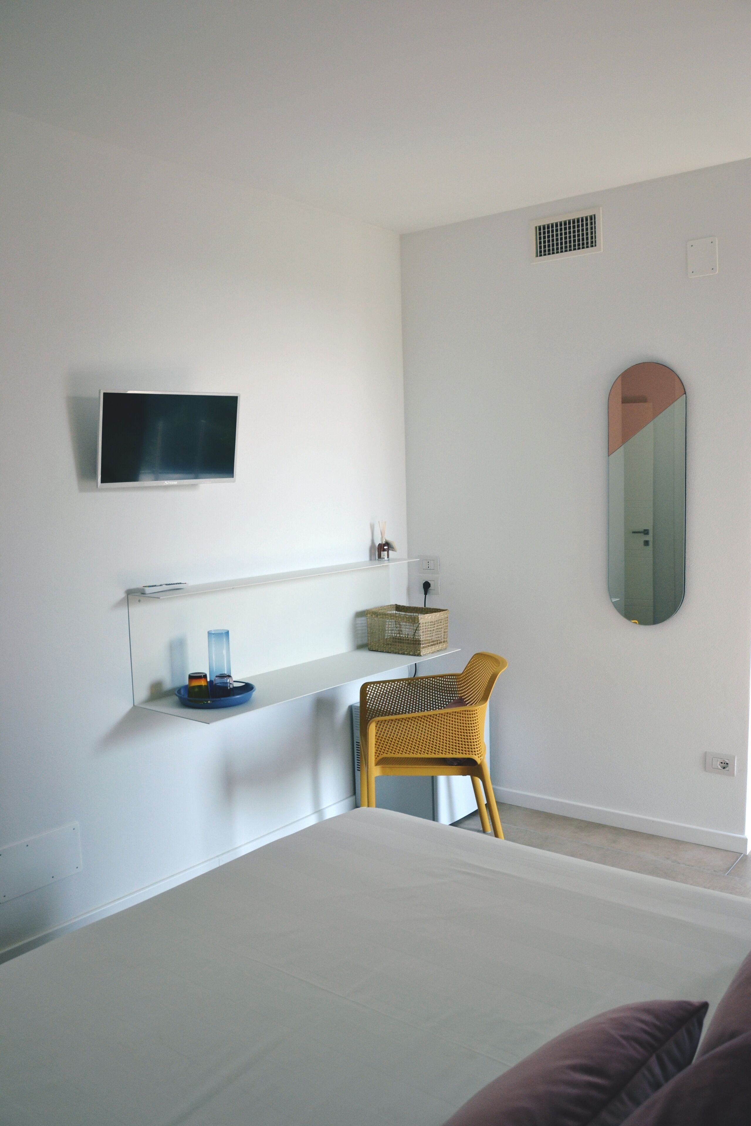 A modern bedroom with a bed, a TV mounted on the wall, a small desk with a chair, and a mirror.