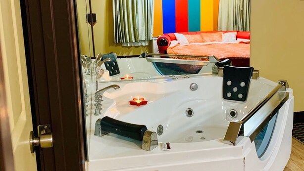 A room with a large white bathtub, a bed with orange bedding, and a colorful wall decoration. - Motor City Inn & Suites (Melvindale)