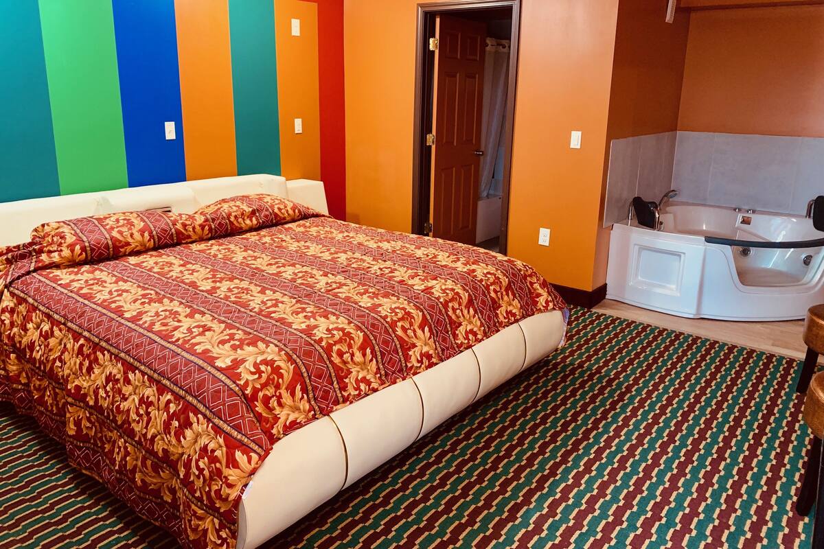 Une chambre d’hôtel avec un grand lit, une salle de bain avec baignoire et un décor mural aux couleurs vives.