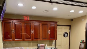 A hotel reception area with marble counters, wooden cabinets, and a security camera. - Motor City Inn & Suites (Melvindale)