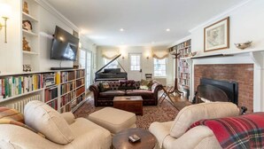 A living room with a piano, sofas, a fireplace, and bookshelves.