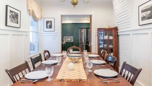 A dining room with a wooden table set for six, flanked by chairs. A chandelier hangs from the ceiling, and there are framed pictures on the walls.