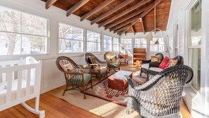 A sunlit room with wooden beams, wicker furniture, and large windows.