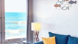 Ein Zimmer mit Meerblick, ein blaues Sofa mit gelbem Kissen, ein Glastisch und eine Lampe.