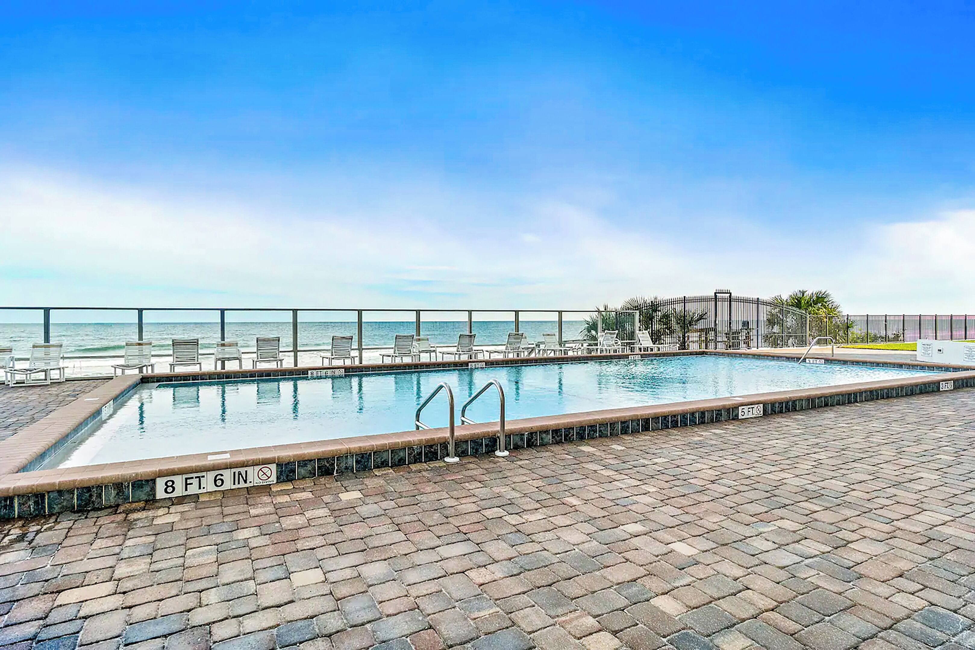 A rectangular pool with a brick border, lounge chairs, and a railing.