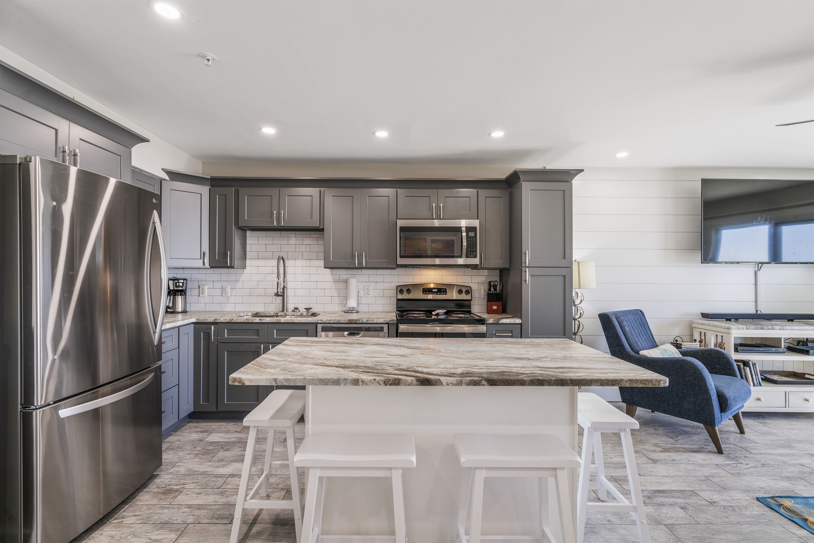 A modern kitchen with stainless steel appliances, grey cabinets, and a marble island with bar stools.
