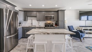 A modern kitchen with stainless steel appliances, grey cabinets, and a marble island with bar stools. - Ground Floor Gulf Front Oasis On Crystal Beach (Destin)