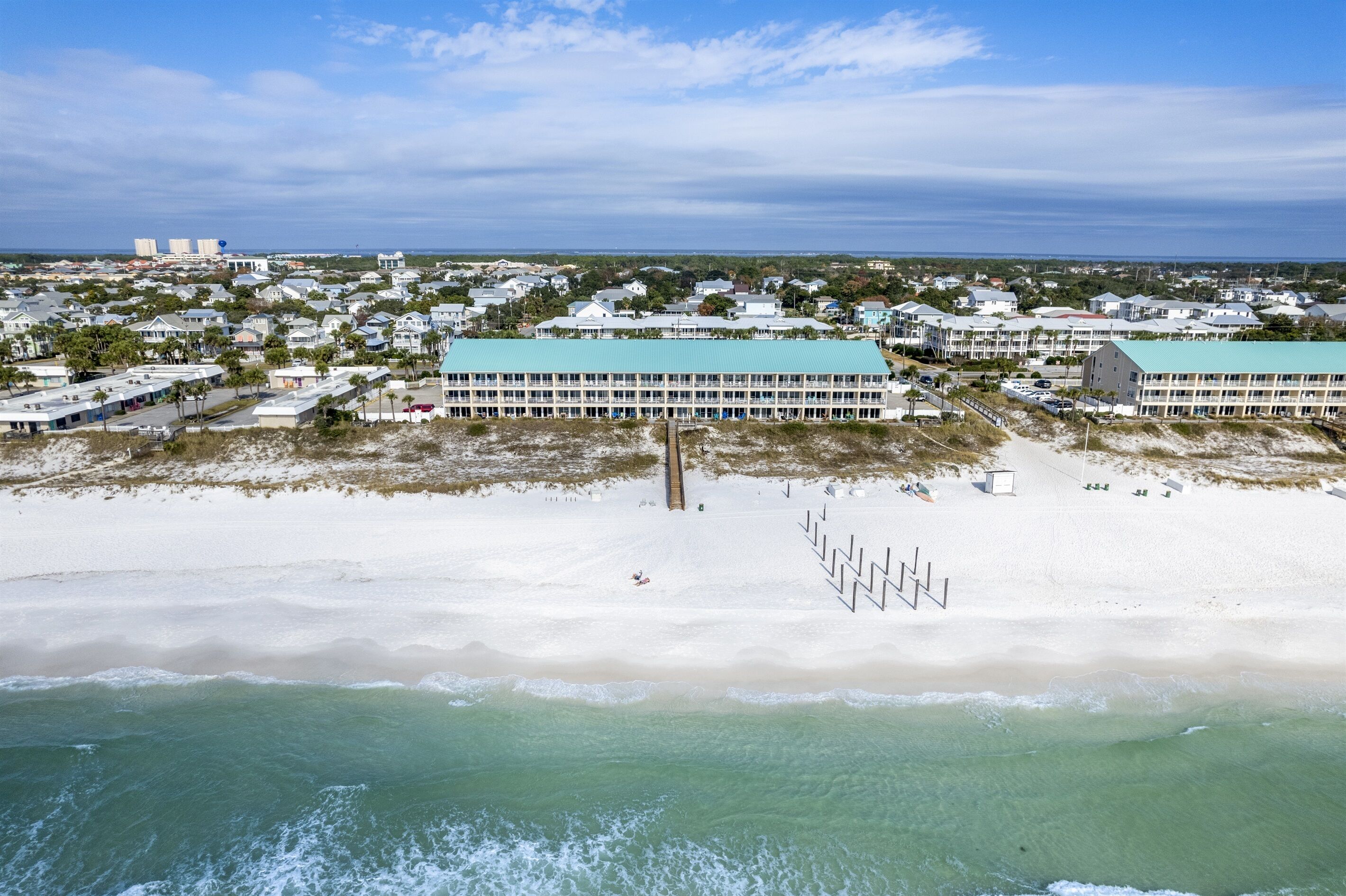 Vue aérienne d’un hôtel situé sur la côte, composé de plusieurs bâtiments, avec une plage de sable et une vue dégagée sur l’océan.