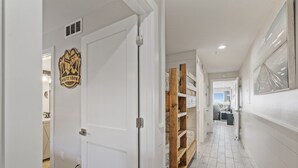 A hallway with a white door, a wooden shelf unit, and a framed artwork on the wall. - Ground Floor Gulf Front Oasis On Crystal Beach (Destin)