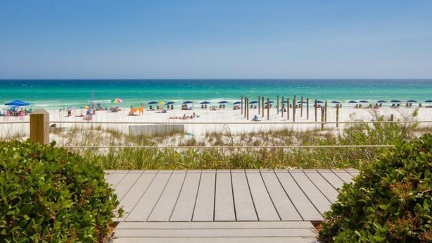 A beach with a wooden walkway leading to the shore, surrounded by greenery. - Ground Floor Gulf Front Oasis On Crystal Beach (Destin)