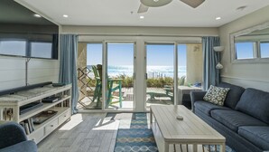 A modern living room with a sofa, coffee table, and TV stand. A ceiling fan and large windows provide natural light and a view of the ocean. - Ground Floor Gulf Front Oasis On Crystal Beach (Destin)